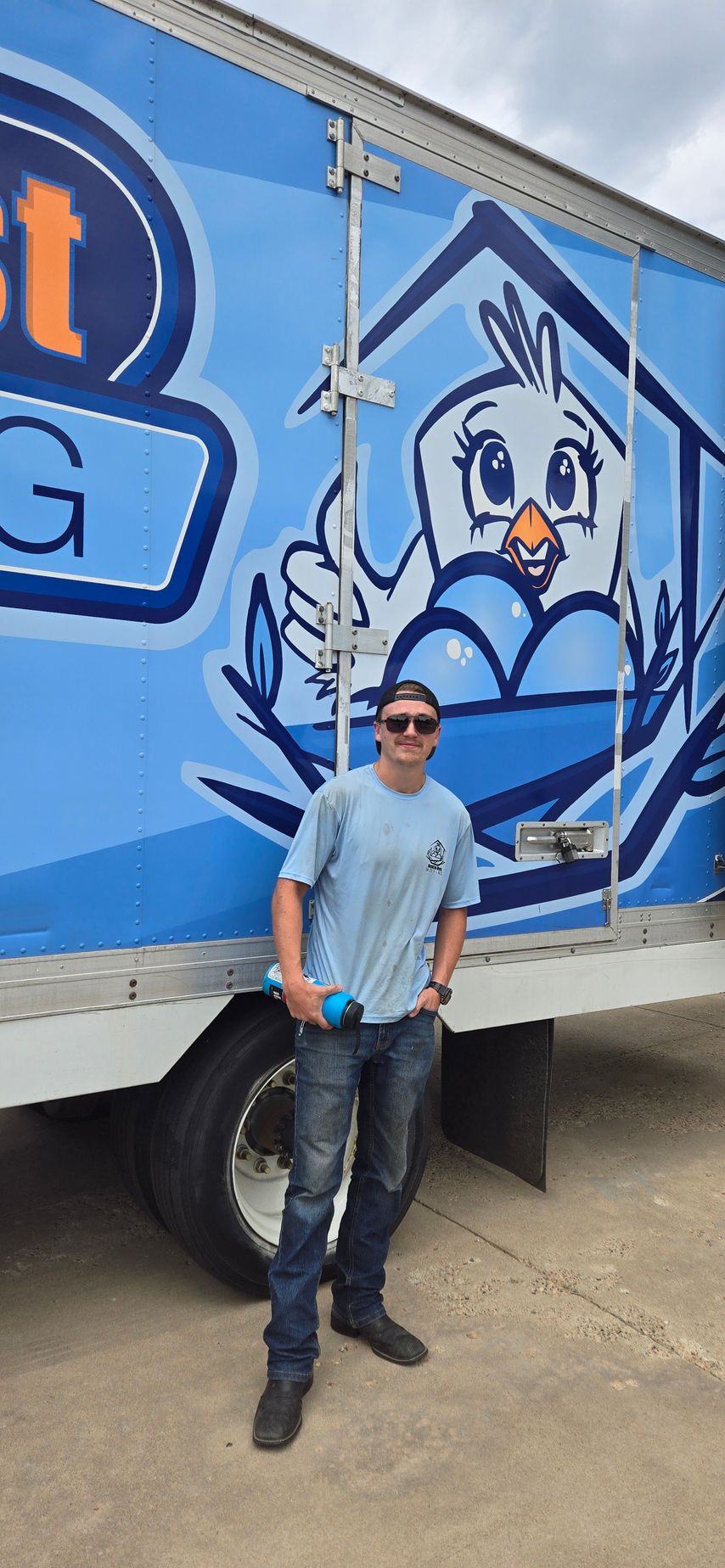 A man is standing in front of a blue truck with a chicken on the side.