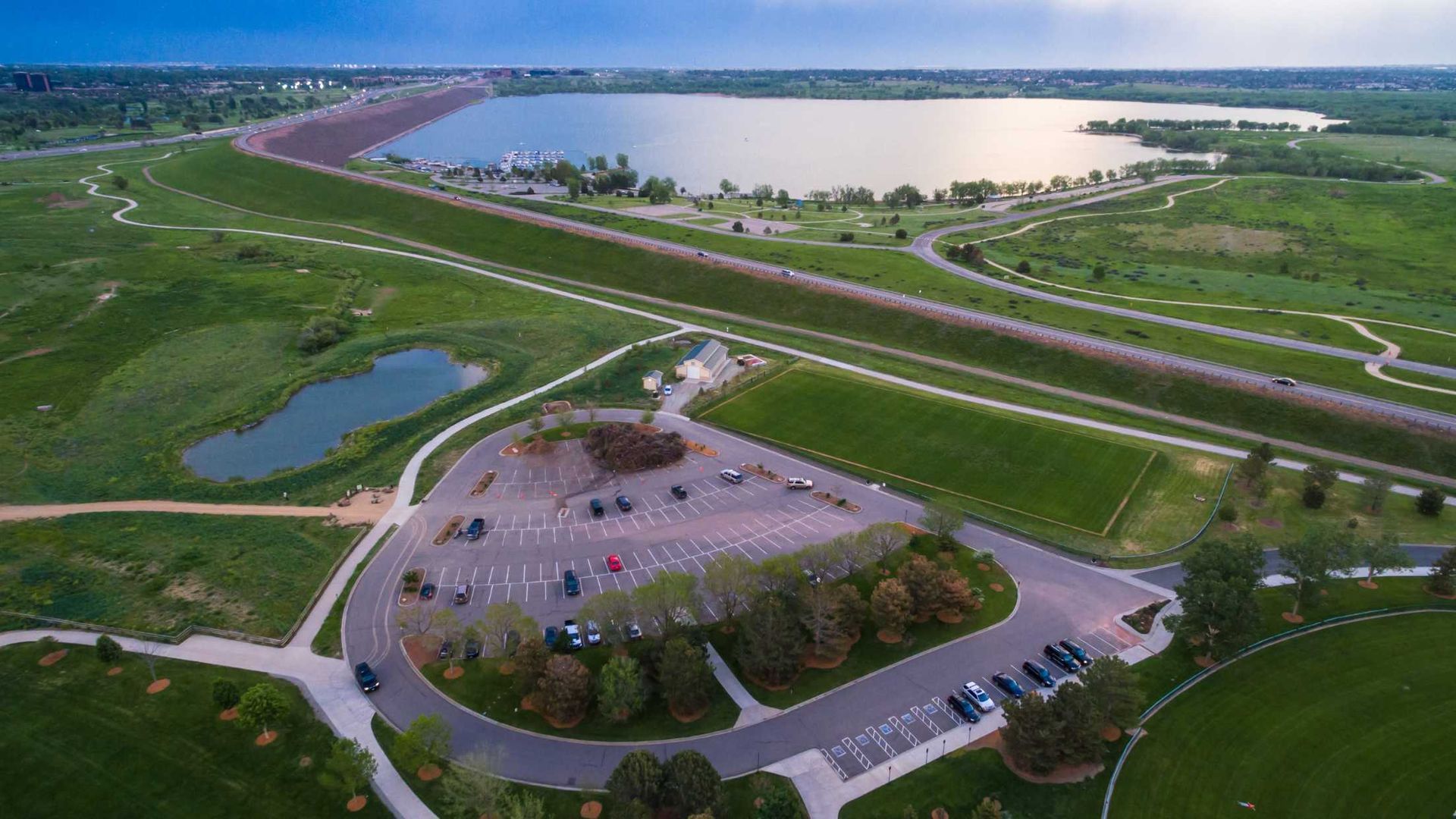 An aerial view of a park with a lake and a parking lot.