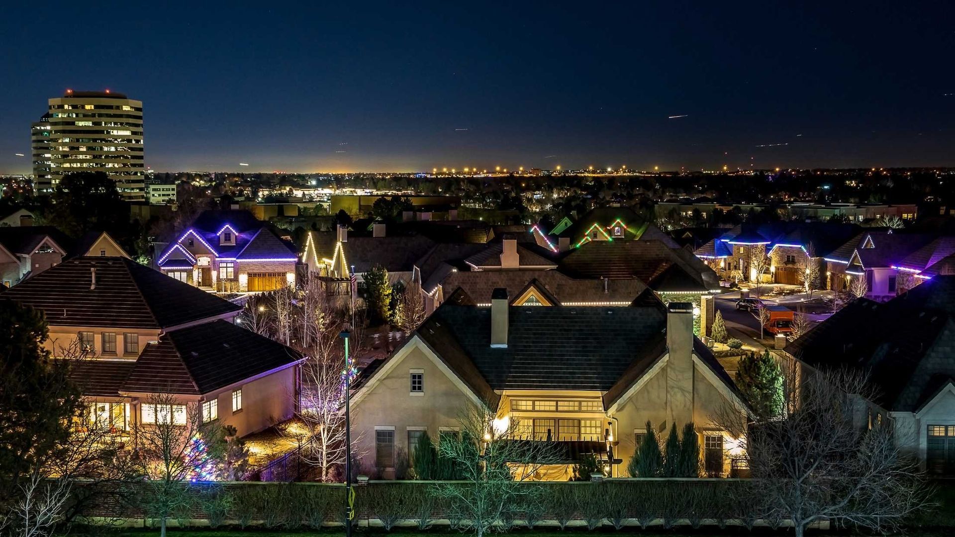 An aerial view of a residential area at night with houses lit up with christmas lights.
