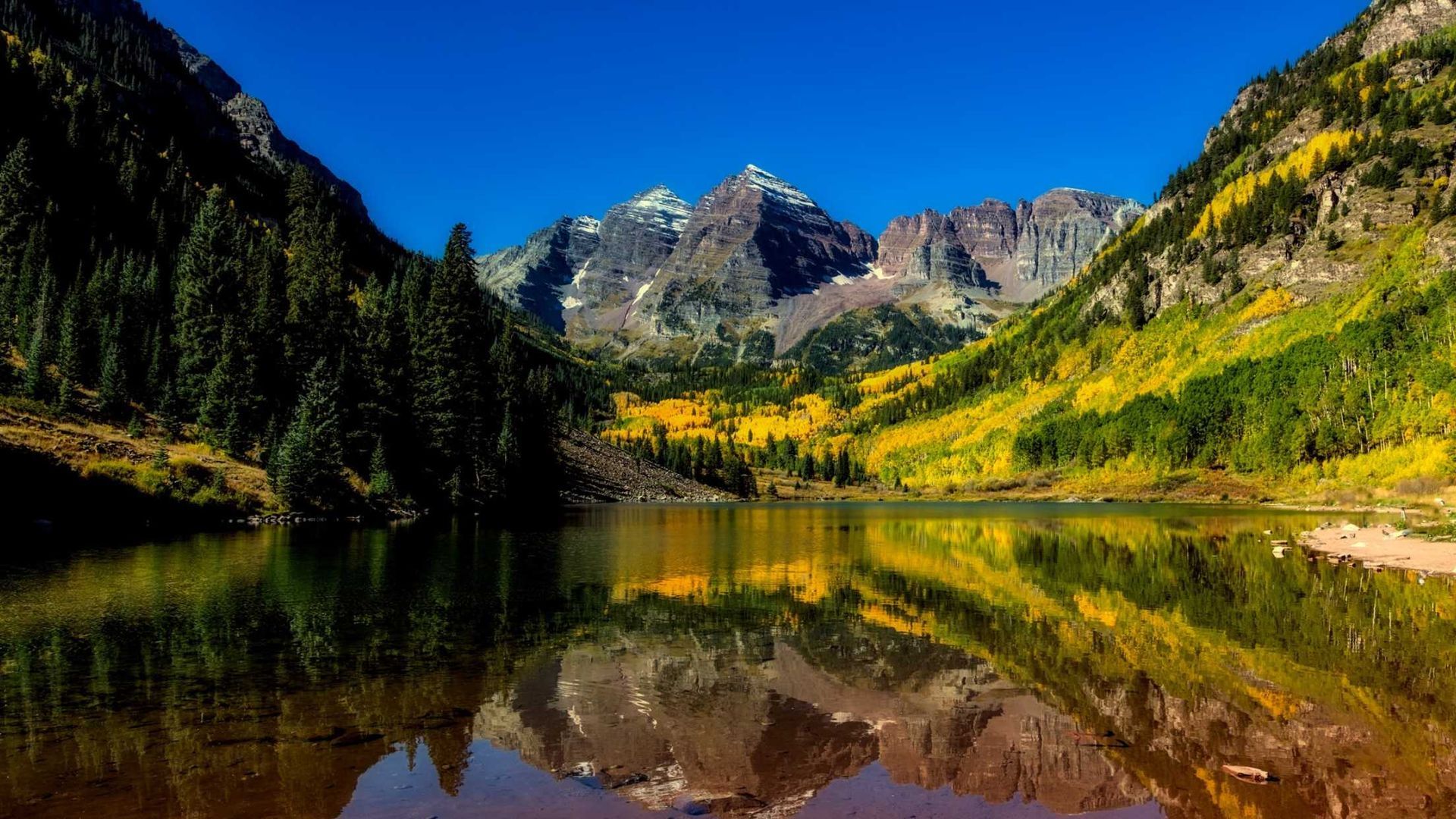 A lake surrounded by mountains and trees with mountains reflected in the water.