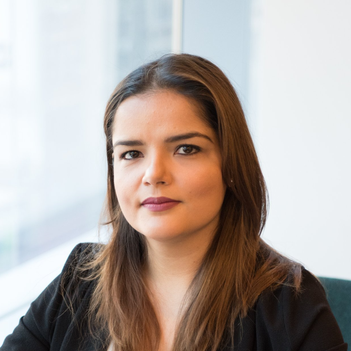 A woman is sitting in front of a window and looking at the camera.
