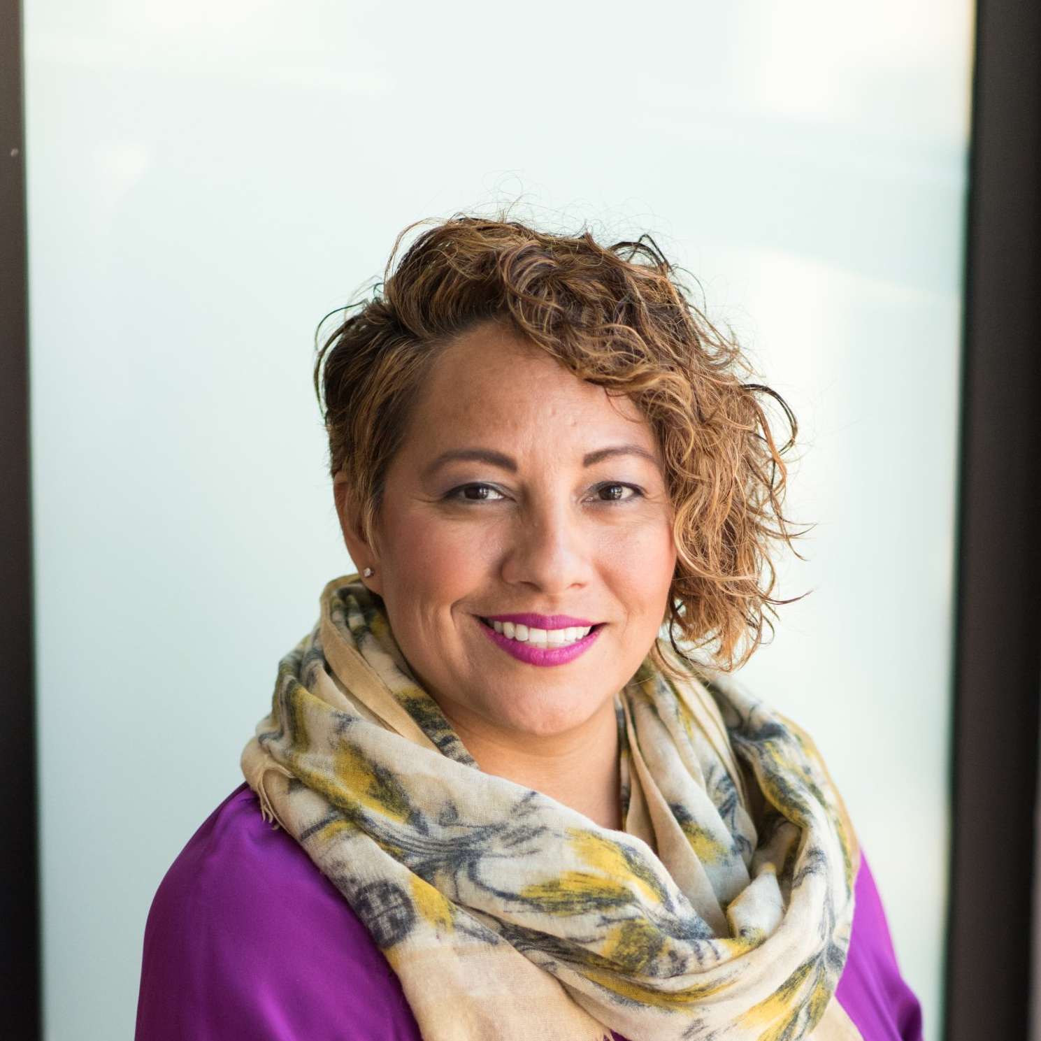 A woman wearing a purple shirt and a scarf is smiling for the camera.