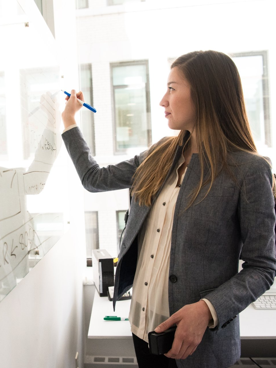 A woman is writing on a whiteboard with a pen.