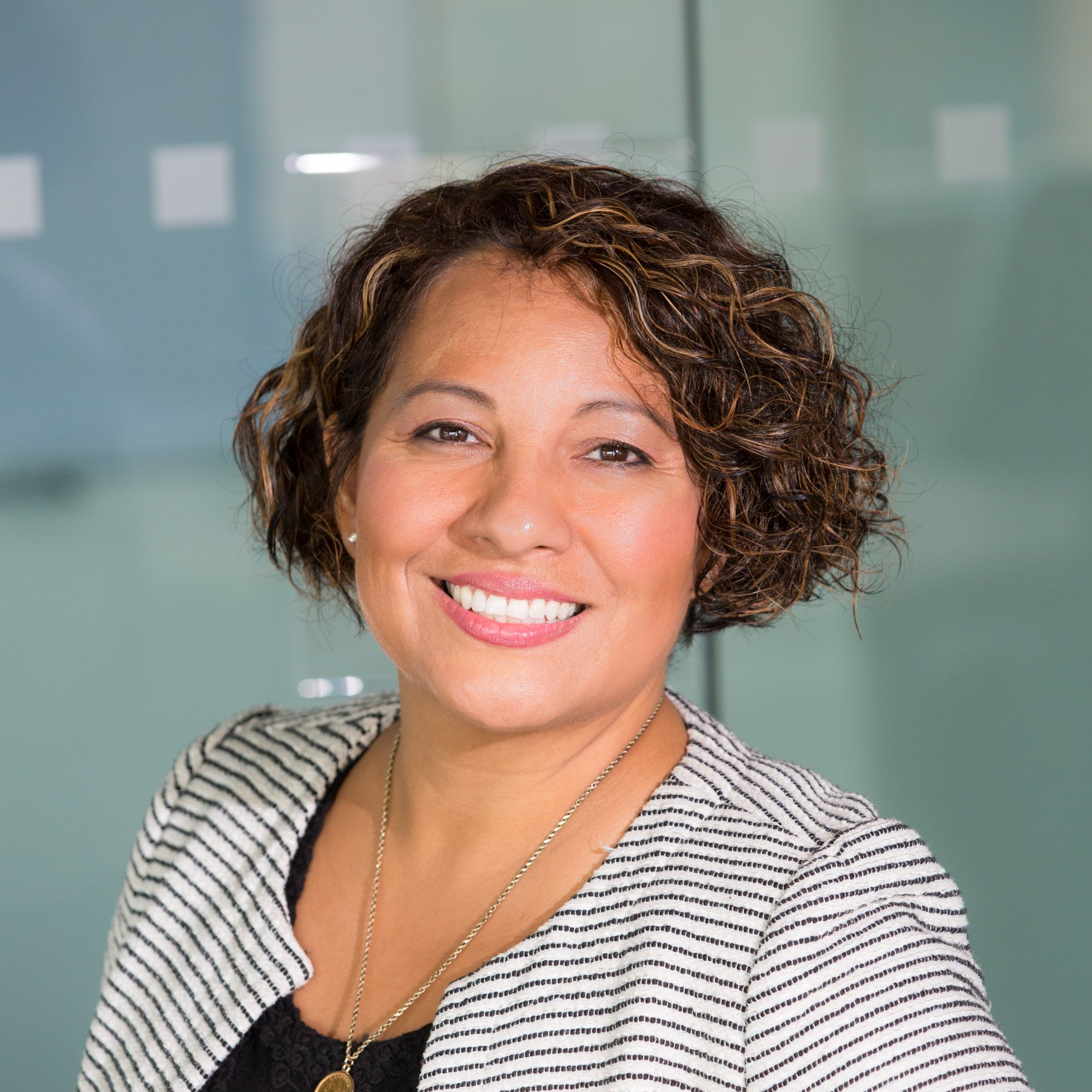 A woman wearing a striped jacket and a necklace is smiling for the camera.
