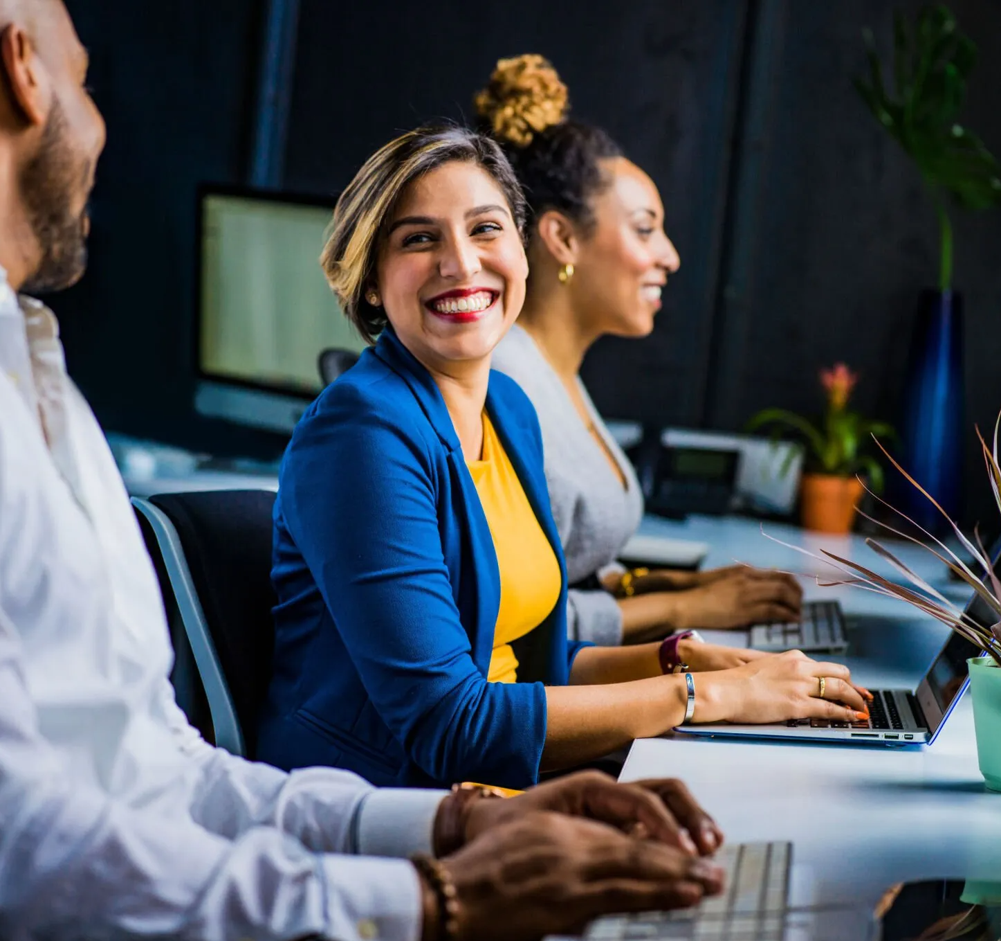 A group of people are sitting at a table with laptops and smiling.