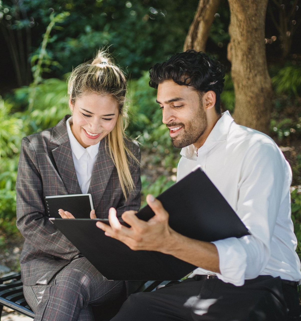 A man and a woman are sitting on a bench looking at a folder