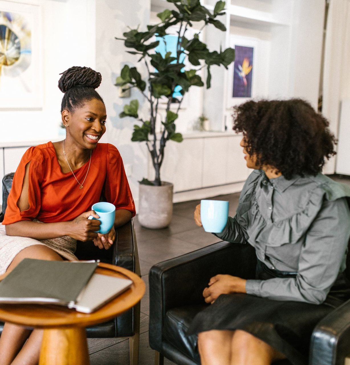 Two women are sitting in chairs talking and drinking coffee.
