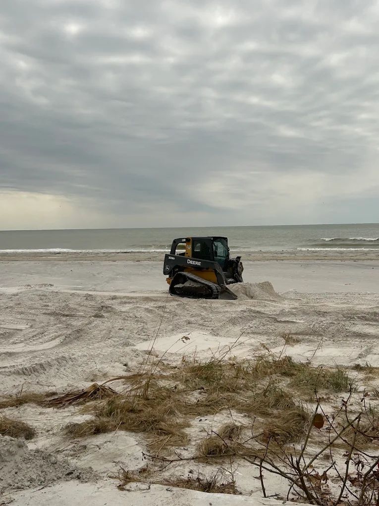 A yellow and black skid-steer loader parked on a sandy beach under a cloudy sky.