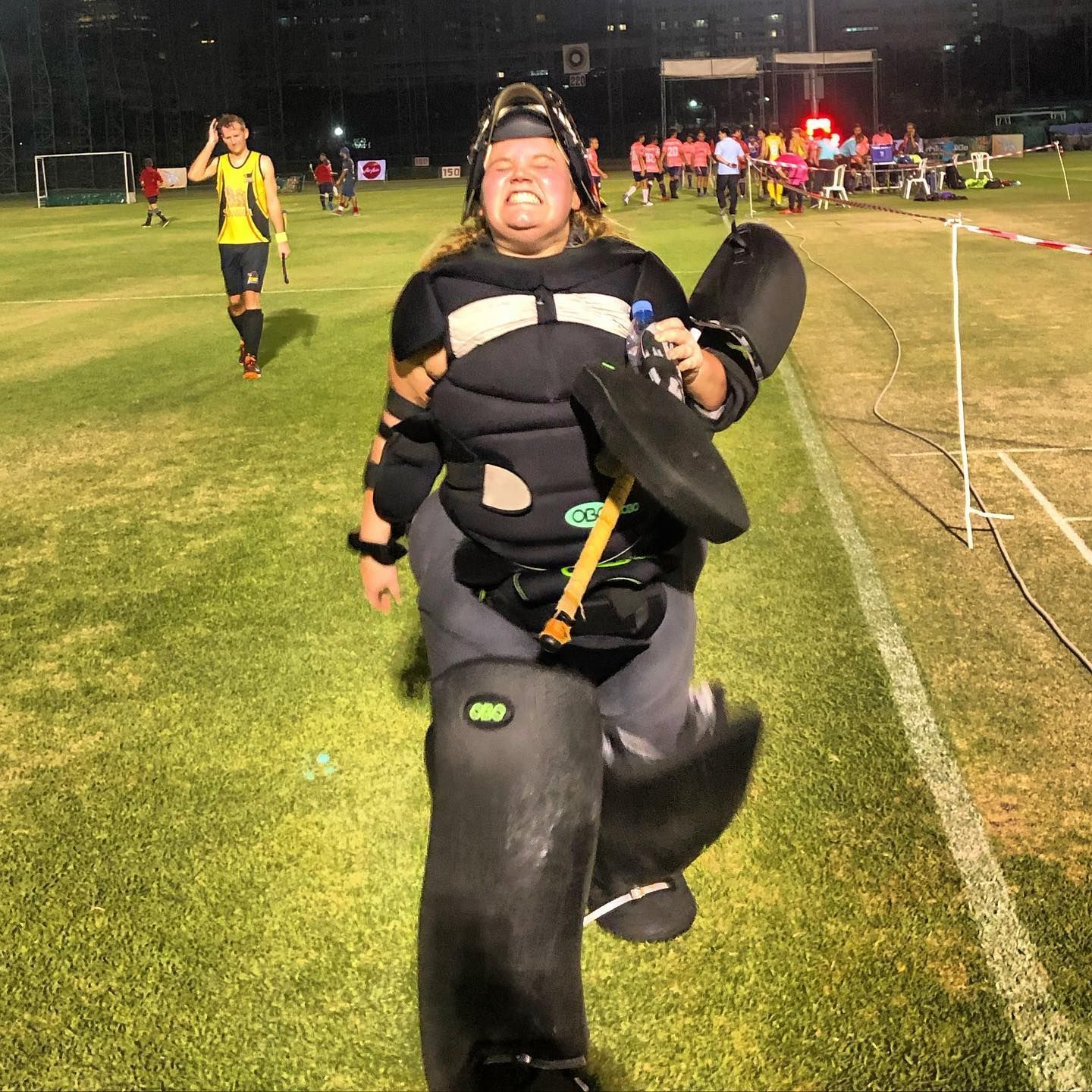 A woman in a catcher 's uniform is holding a bat on a field
