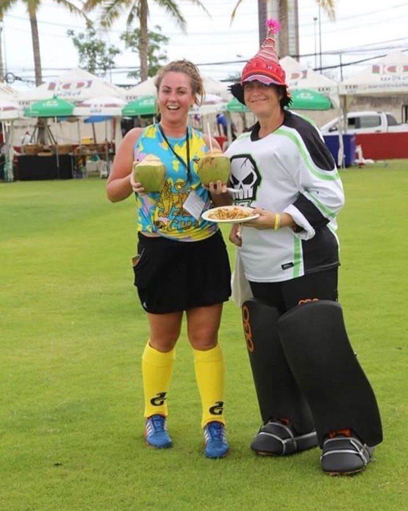 Two women are standing on a grassy field holding plates of food and drinks