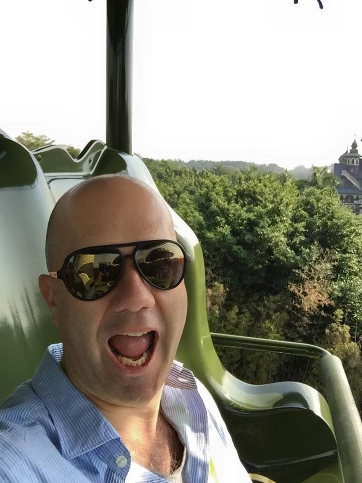 A bald man wearing sunglasses is sitting in a chair with his mouth open.