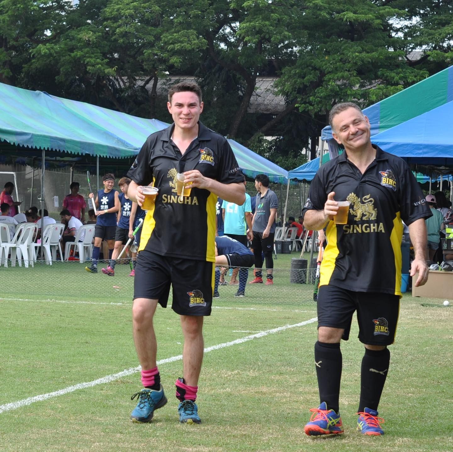 Two men wearing singha shirts are walking on a field