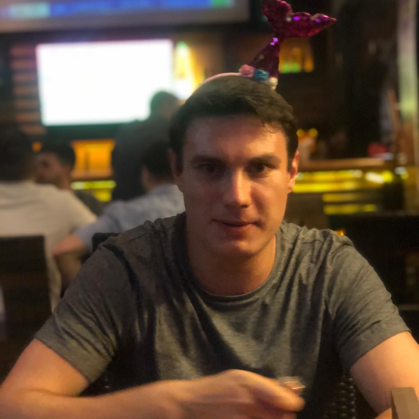 A man wearing a mermaid headband sits at a table