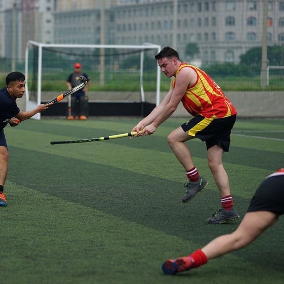 A man in a red and yellow shirt is holding a hockey stick