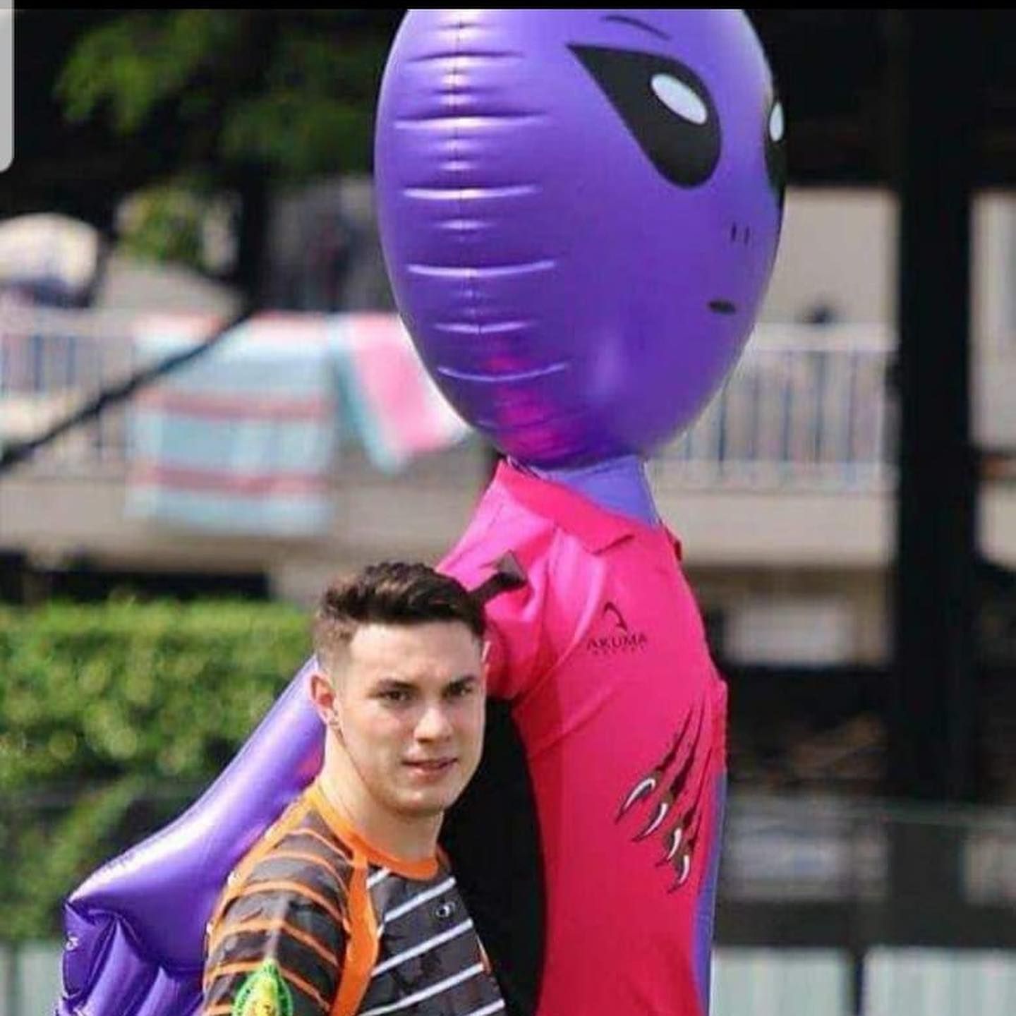 A man is standing next to a purple inflatable alien