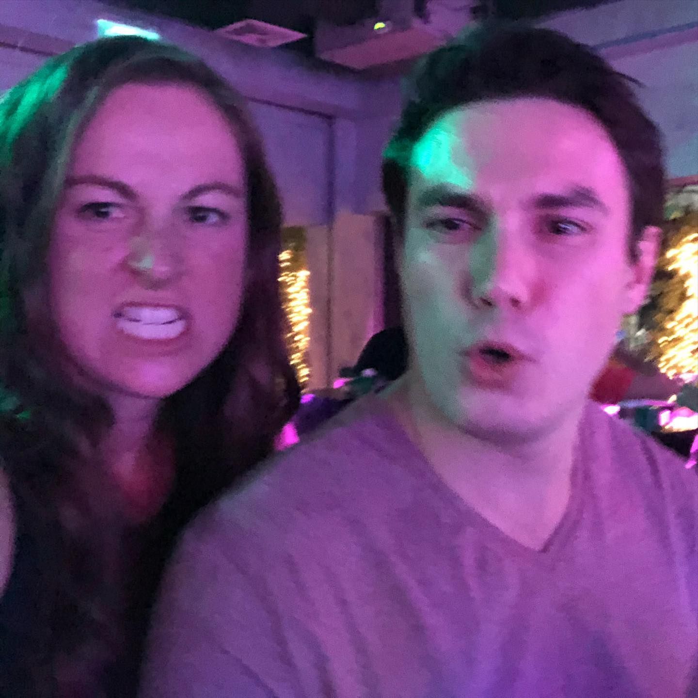 A man and a woman are posing for a picture in a room with purple lights.