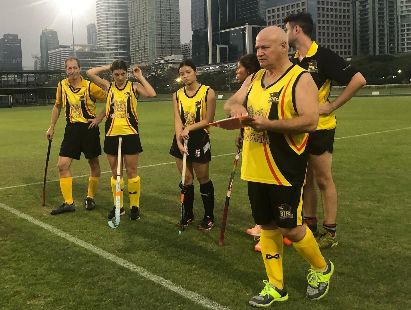 A group of people standing on a field with a man holding a clipboard.