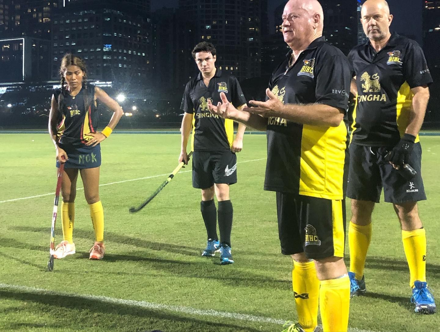 A group of people are standing on a field holding hockey sticks.