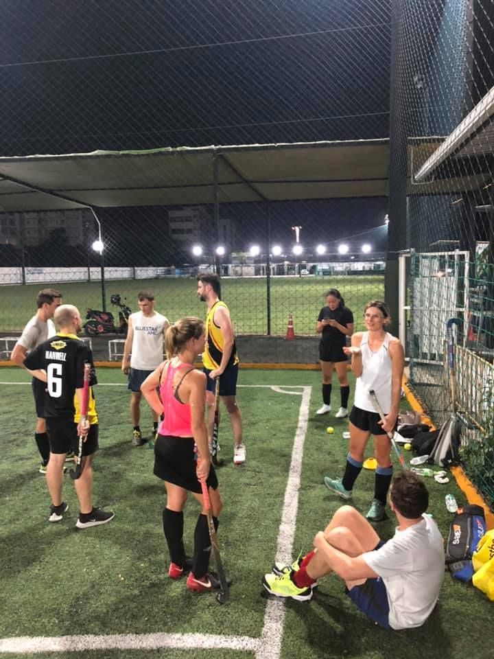 A group of people are standing and sitting on a soccer field at night.