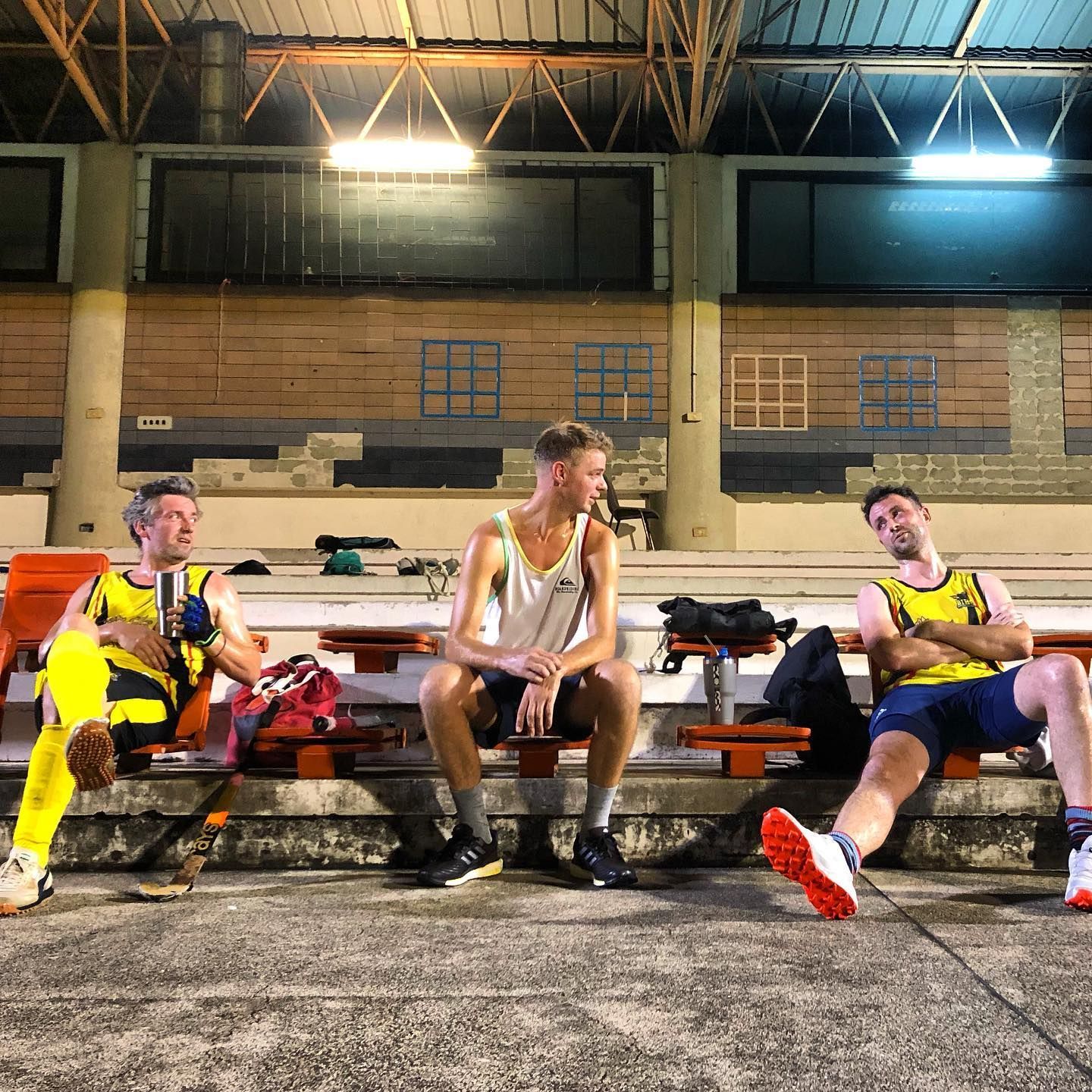 Three men are sitting on a bench in front of a building.