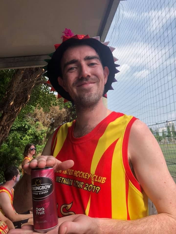 A man wearing a hat and a tank top is holding a can of beer.