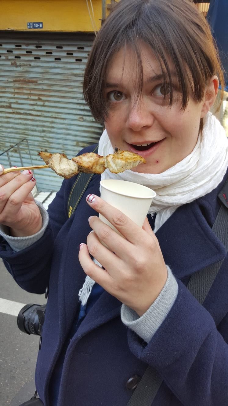 A woman is eating a skewer of food from a paper cup.