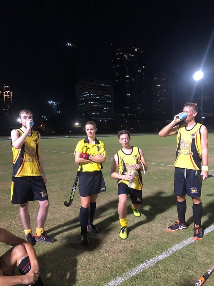 A group of people are standing on a field at night drinking water.