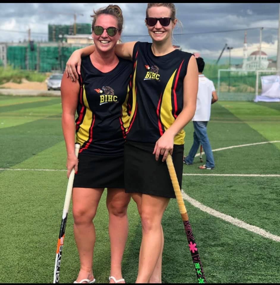 Two female hockey players are posing for a picture on a field