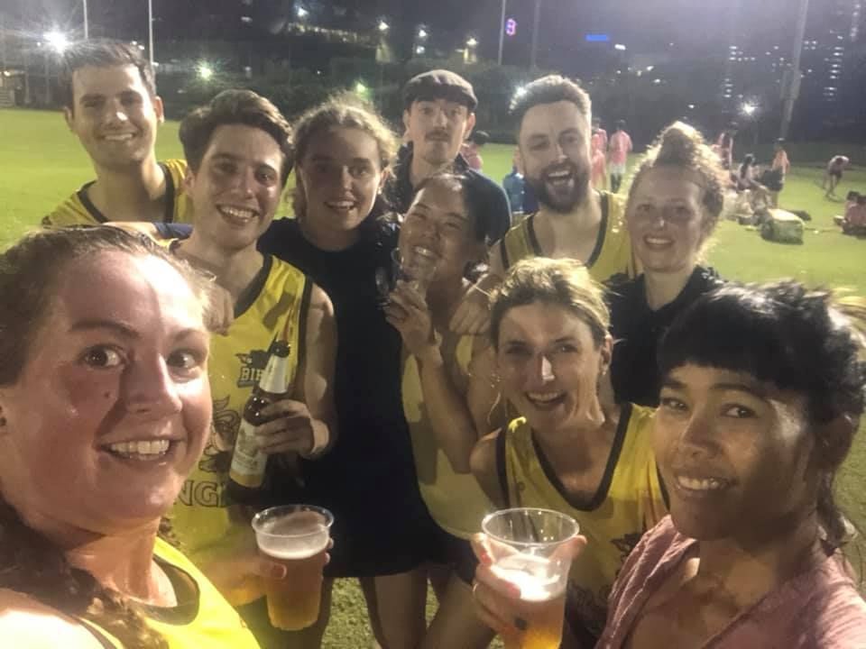 A group of people are standing next to each other on a field holding cups of beer.