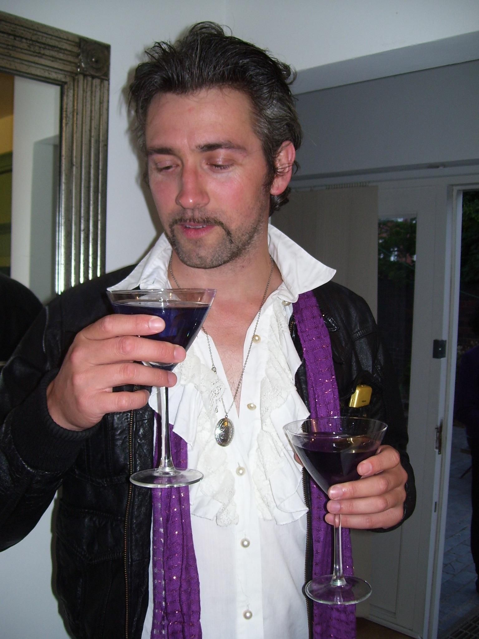 A man wearing a purple scarf is holding two martini glasses