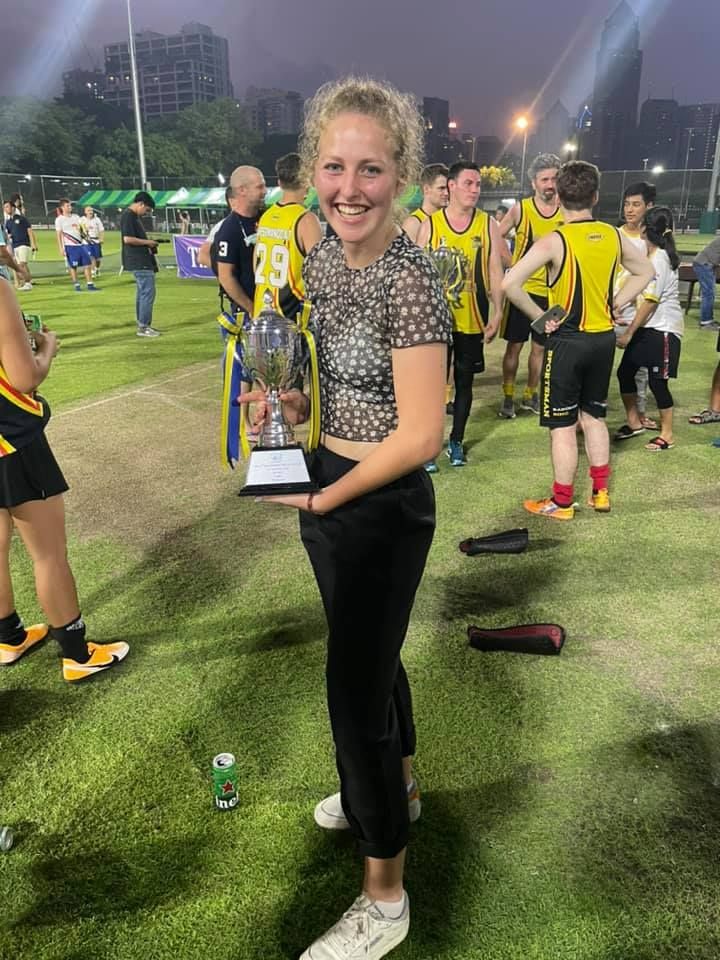 A woman is holding a trophy in front of a group of people on a field.