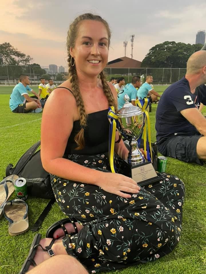 A woman is sitting on the grass holding a trophy.