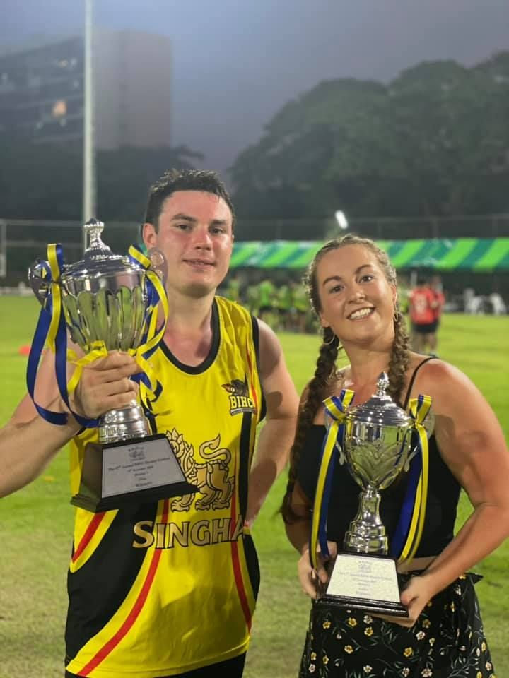 A man and a woman are holding trophies on a field.
