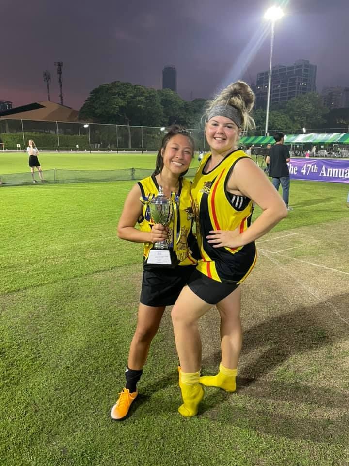 Two women are standing next to each other on a field holding a trophy.