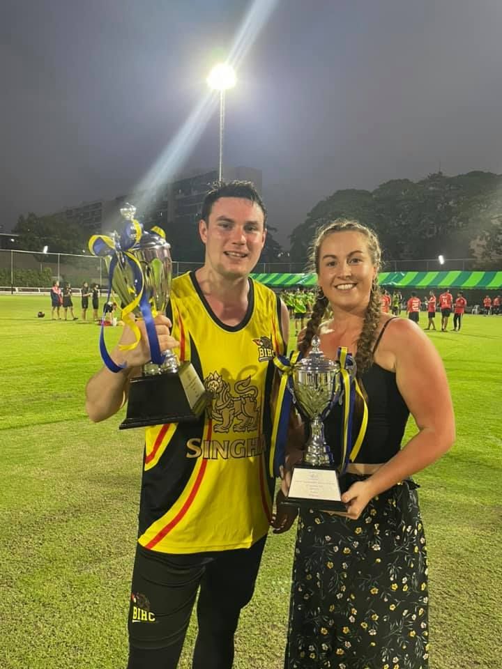 A man and a woman holding trophies on a field