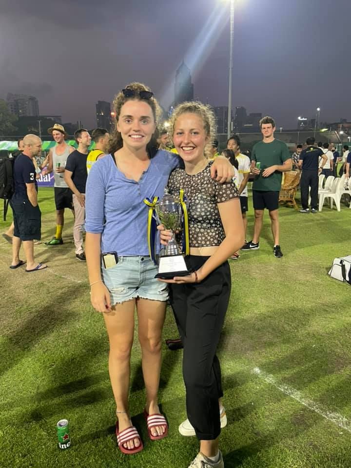 Two women are standing next to each other on a field holding a trophy.