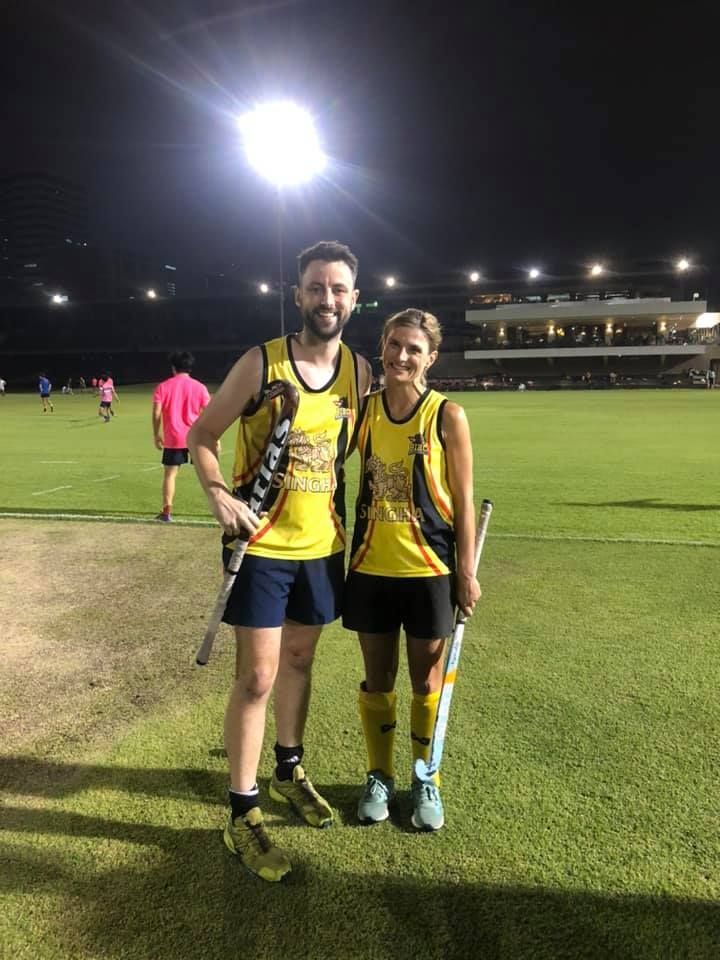 A man and a woman are standing next to each other on a field holding hockey sticks.
