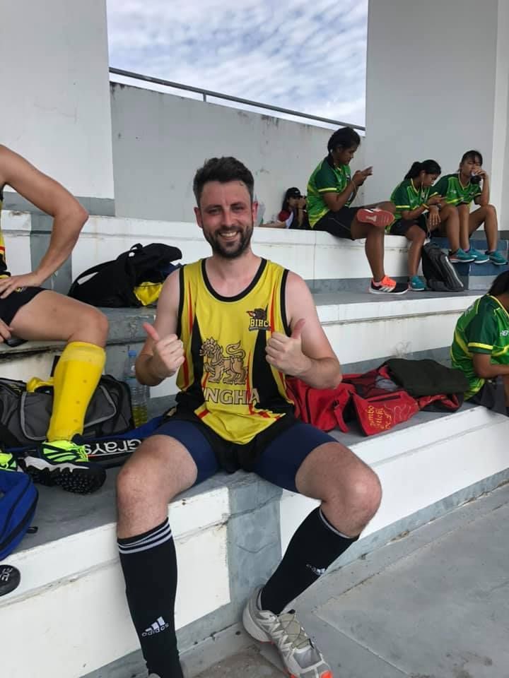 A man in a yellow tank top is giving a thumbs up