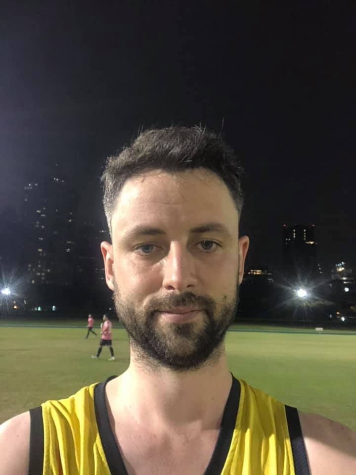 A man with a beard is wearing a yellow tank top.