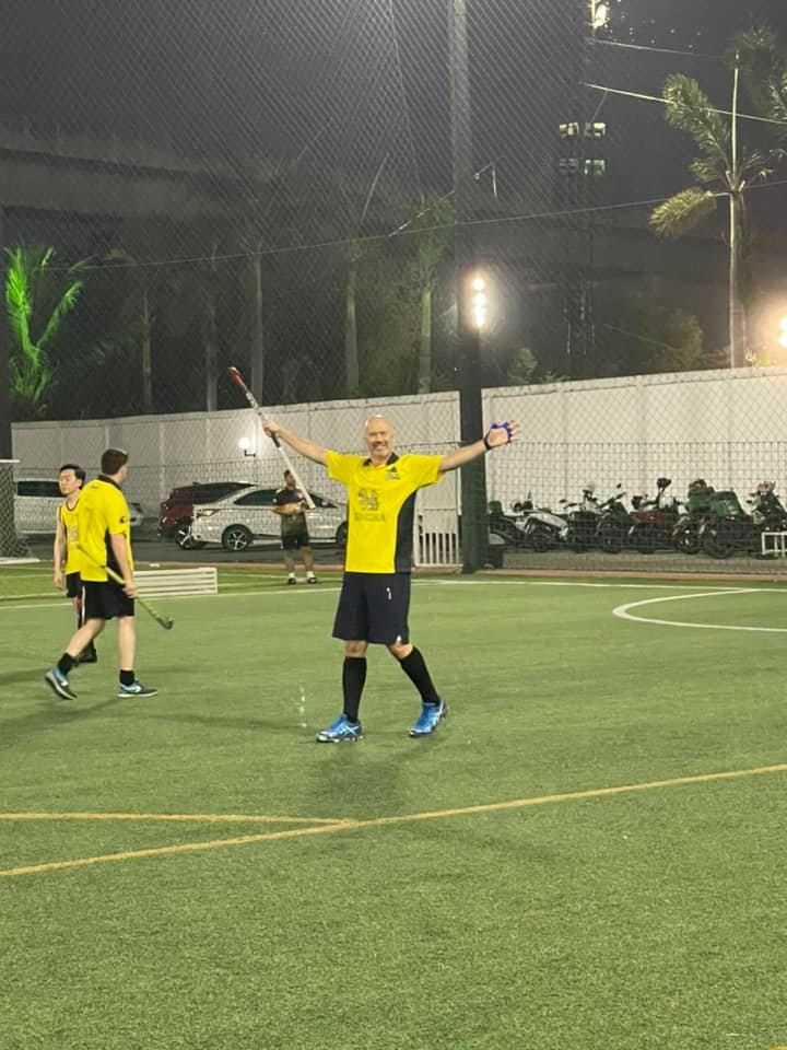 A man in a yellow shirt is holding a hockey stick on a field.