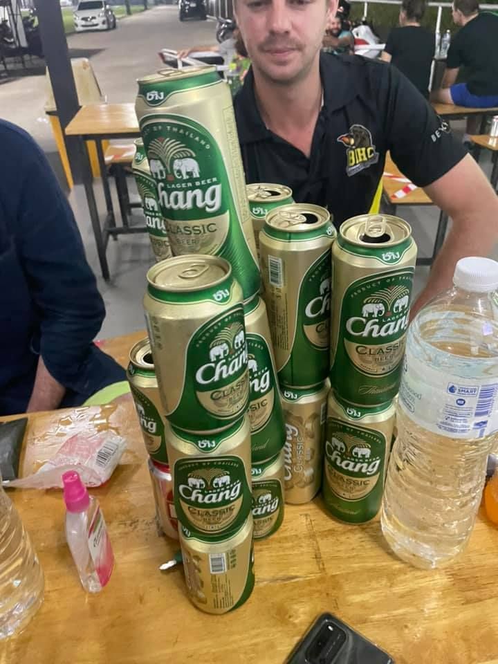 A man is sitting at a table with a stack of chang beer cans.