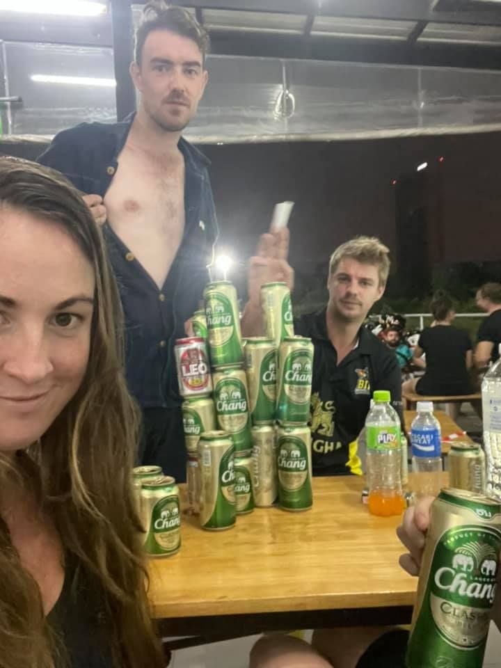 A group of people are sitting at a table holding cans of beer.