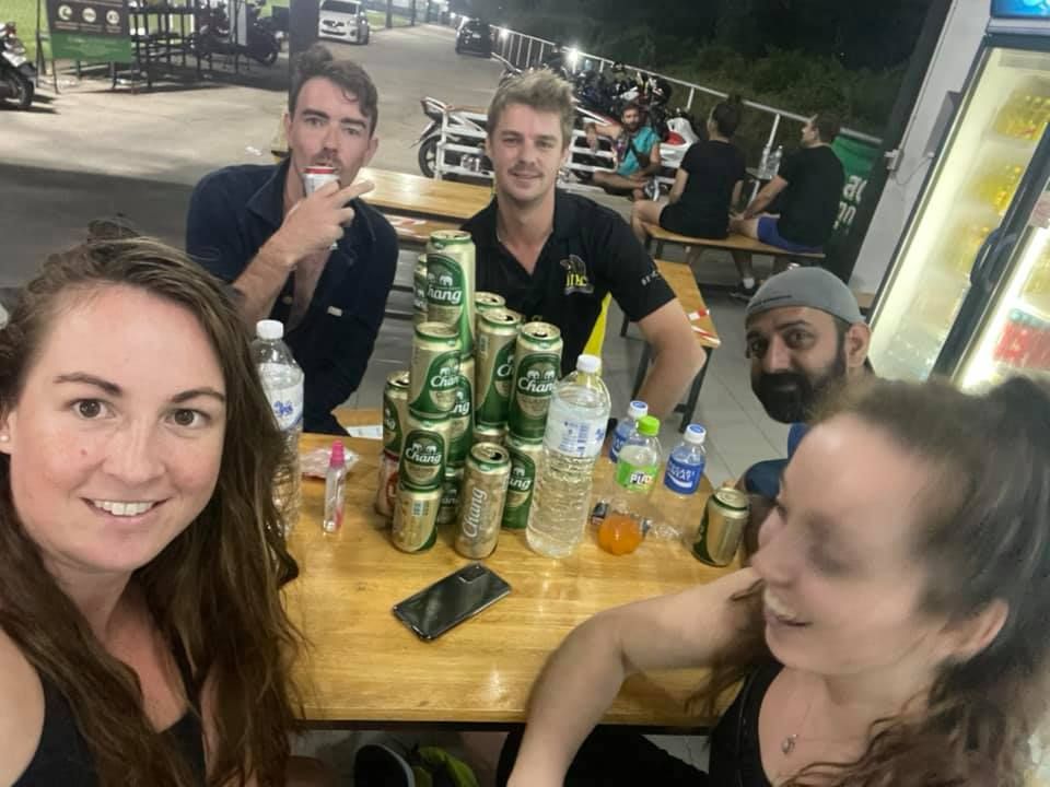 A group of people are sitting at a table with cans of beer on it.
