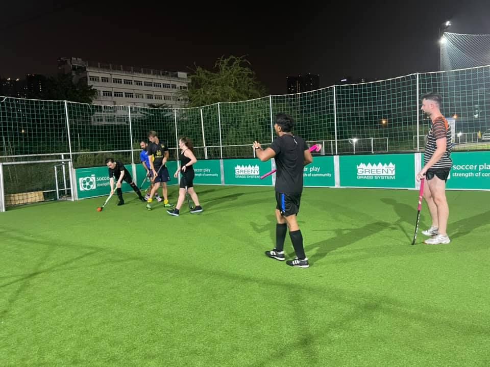 A group of people are playing field hockey on a field at night.