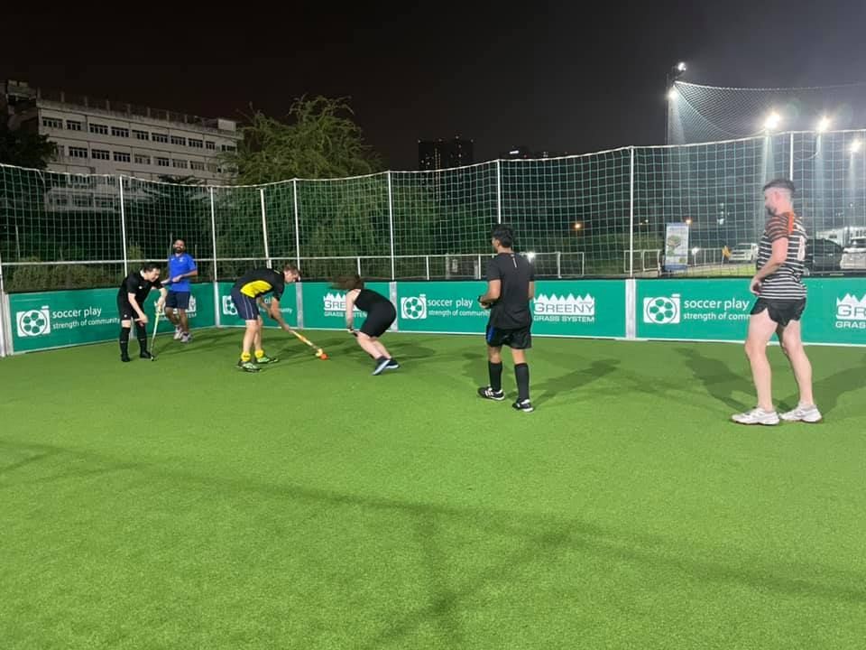 A group of people are playing field hockey on a field at night.