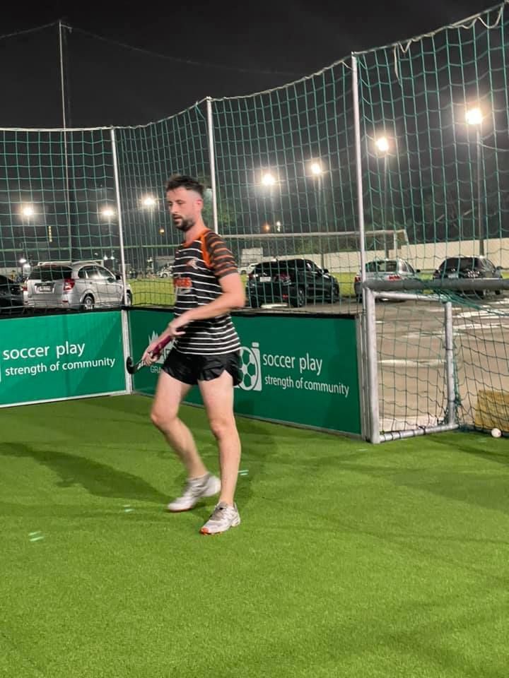A man is standing on a soccer field holding a tennis racket.