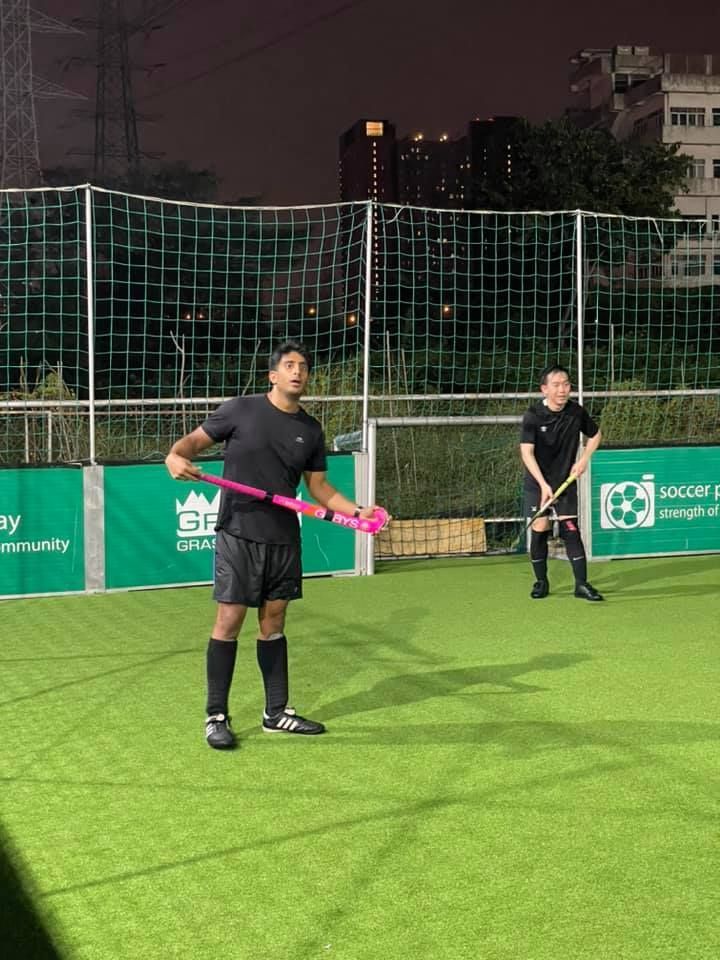 Two men are playing field hockey on a field at night.
