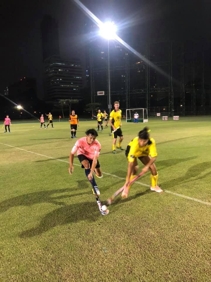 A group of people are playing field hockey on a field at night.