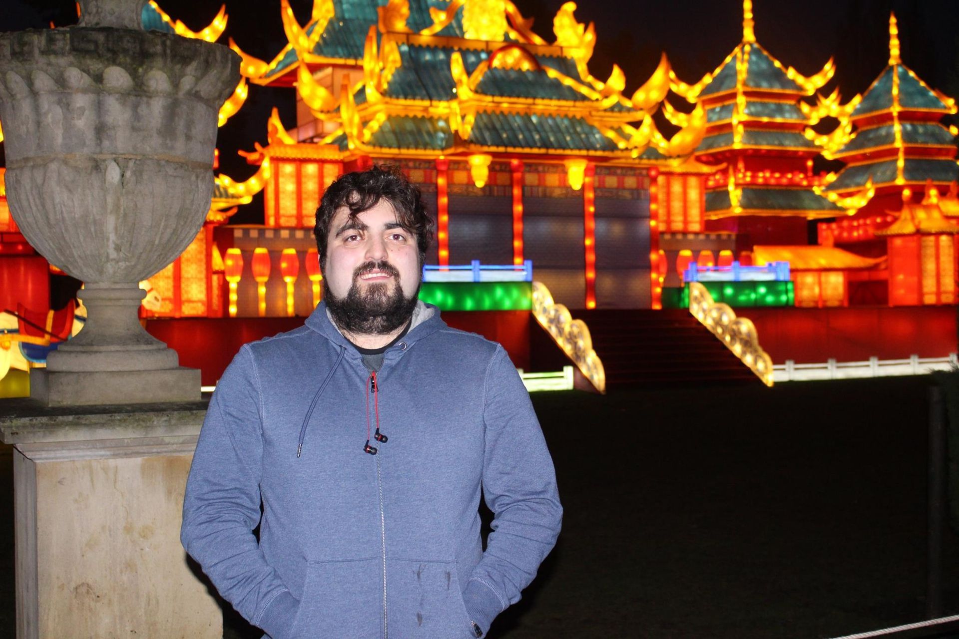 A man with a beard is standing in front of a building that is lit up at night