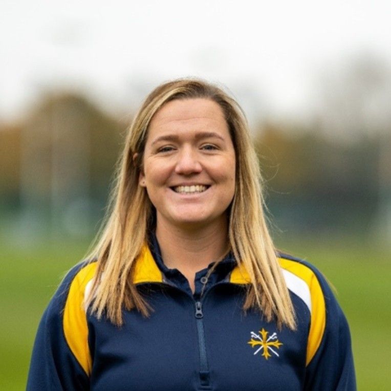 A woman wearing a blue and yellow jacket is smiling for the camera.